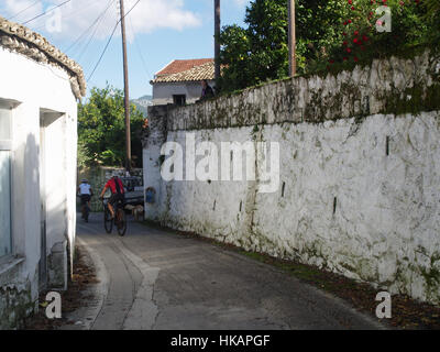 Deux cyclistes vêtus avec équitation à travers la rue grec traditionnel au village Pagi, Corfou, Grèce Banque D'Images