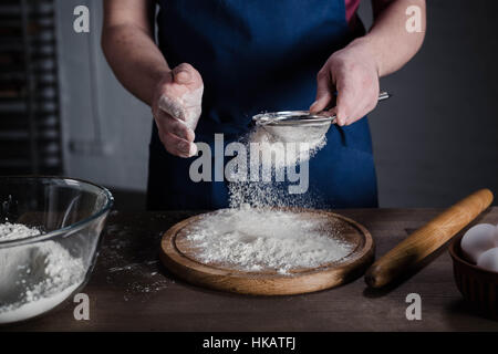 Baker sasser la farine dans la boulangerie, cropped shot Banque D'Images