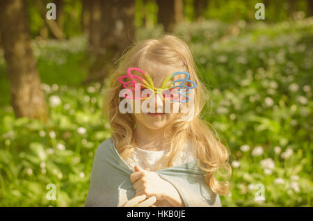 Belle petite fille blonde en verres colorés en vert printemps meadow portrait Banque D'Images