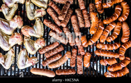 Variété mixte de viande sur le gril du barbecue au charbon. Cevapcici, saucisses, ailes de poulet et des hot-dogs sur le barbecue au charbon de barbecue. Banque D'Images