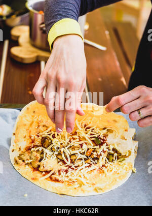 La femme est de faire des plats mexicains traditionnels burrito, fajitas, enchiladas, quesadillas ou les tacos avec le fromage cheddar sur un support papier, lire Banque D'Images