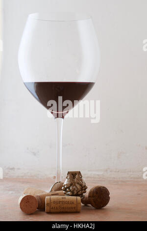 Un grand verre de vin rouge avec un arrangement de bouchons et d'un bouchon de bouteille d'argent à la base Banque D'Images