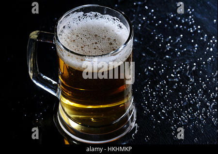 La bière brune en verre noir table sur l'éclat humide Banque D'Images