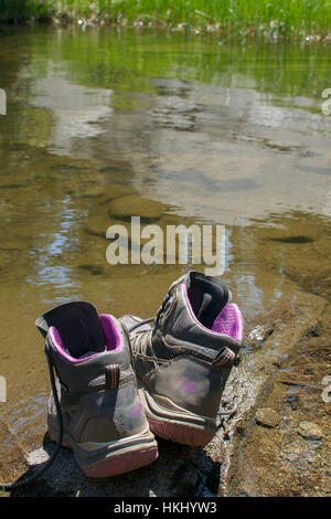 Vieille paire de chaussures de randonnée poussiéreux, sur un rocher à la marge d'un lac, ce qui suggère que son propriétaire s'en nageant - Aventure dans le concept de plein air Banque D'Images