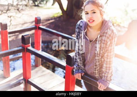 Une jolie adolescente fait une pose ludique sur une promenade dans le parc avec la lumière du soleil par derrière ; New Westminster, Colombie-Britannique, Canada Banque D'Images