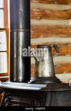 Close up d'un vieux pot de café en métal sur le dessus d'un vieux poêle en fonte en log cabin avec fenêtre en arrière-plan, au sud de Maple Creek ; Alberta, Canada Banque D'Images