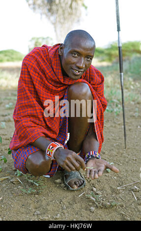 Masaï mâle en vêtements traditionnels Shuka, assis sur le sol, le parc national de Tsavo Ouest, comté de Taita-Taveta, Kenya Banque D'Images