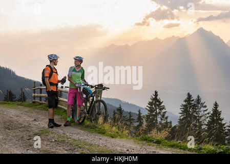 Jeune couple de cyclistes de montagne debout sur chemin de terre pendant le coucher du soleil, Zillertal, Tyrol, Autriche Banque D'Images