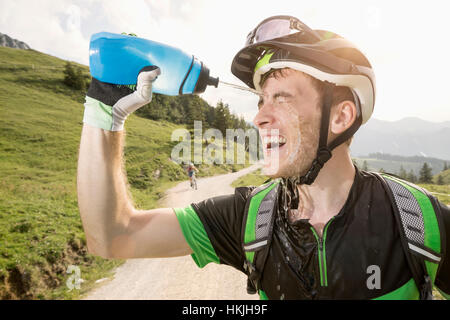 Mountain biker verser de l'eau sur son visage, Bavière, Allemagne, Kampenwand Banque D'Images