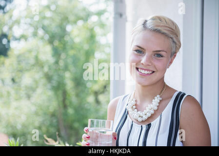 Portrait d'une jeune femme l'eau potable sur le balcon et souriant, Bavière, Allemagne Banque D'Images