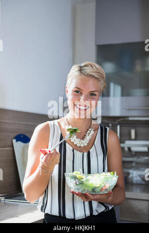 Young woman eating salad dans la cuisine et souriant, Bavière, Allemagne Banque D'Images