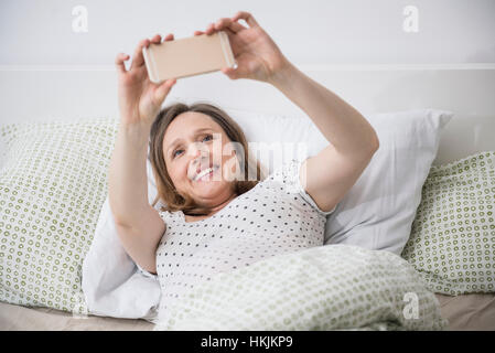 Pregnant woman Lying in Bed et en tenant le téléphone mobile selfies, Munich, Bavière, Allemagne Banque D'Images