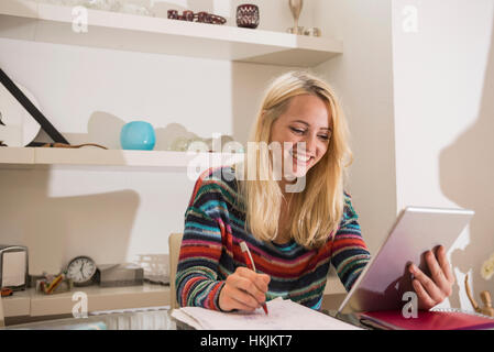 Jeune étudiant fait ses devoirs avec tablette numérique dans la salle de séjour, Bavière, Allemagne Banque D'Images
