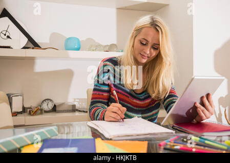 Jeune étudiant fait ses devoirs avec tablette numérique dans la salle de séjour, Bavière, Allemagne Banque D'Images