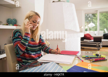 Jeune étudiant à faire leurs devoirs avec un téléphone mobile dans la salle de séjour, Bavière, Allemagne Banque D'Images