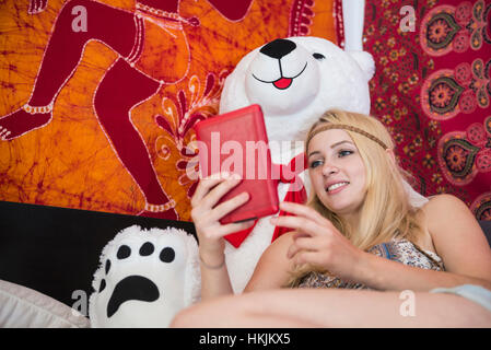 Beau young woman using digital tablet appuyé contre un gros ours en peluche dans la chambre à coucher, Bavière, Allemagne Banque D'Images