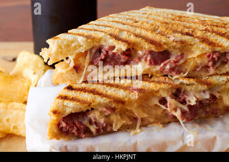 Un sandwich panini grillé avec de la viande et de la fonte du fromage. Le sandwich est coupé et empilé devant une bouteille de bière et croustilles de pommes de terre. Banque D'Images