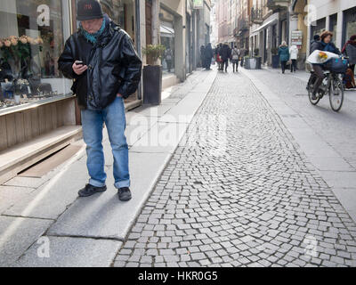 Un vieil homme lecture d'un message texte sur son téléphone cellulaire dans la rue Banque D'Images
