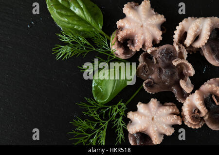 La préparation des fruits de mer dans la cuisine gastronomique avec la crevette rose et pieuvres entouré de fines herbes et épices sur fond noir en noir Banque D'Images