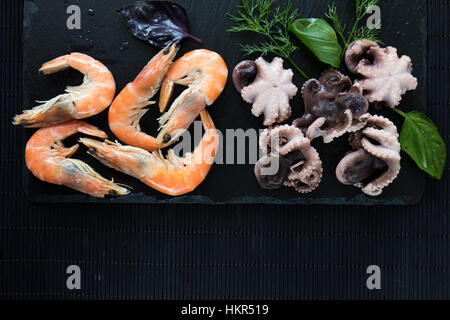 La préparation des fruits de mer dans la cuisine gastronomique avec la crevette rose et pieuvres entouré de fines herbes et épices sur fond noir en noir Banque D'Images