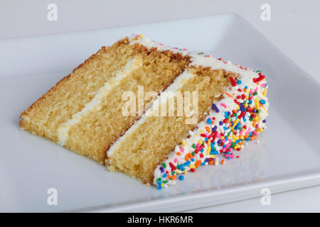 Une tranche de gâteau avec glaçage jaune blanc et saupoudre sur une plaque carrée blanche. Banque D'Images