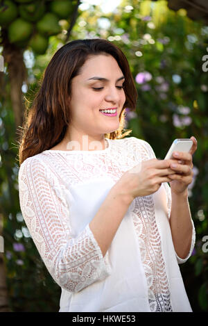 Sourire fille hispanique à l'aide du smartphone sur le green park Banque D'Images