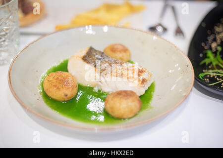 Bol circulaire rustique élégant avec plaque poisson merlu cuit avec sauce verte et petite balle patates sur nappe blanche en restaurant Banque D'Images