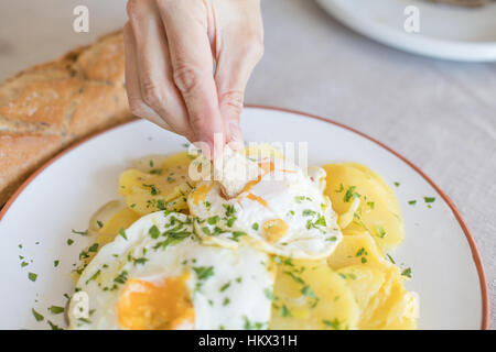 Femme part avec morceau de pain frit trempant dans de l'œuf œuf d'une cuisine typiquement espagnole, avec des tranches de pommes de terre sautées, et le persil haché Banque D'Images