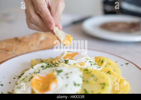 Femme part avec morceau de pain frit trempant dans de l'œuf œuf d'une cuisine typiquement espagnole, avec des tranches de pommes de terre sautées, et le persil haché Banque D'Images