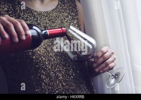Close up of Caucasian horizontale femme retro vintage robe paillette d'or en elle-même de verser le vin rouge dans un grand verre à boire près d'une fenêtre Banque D'Images