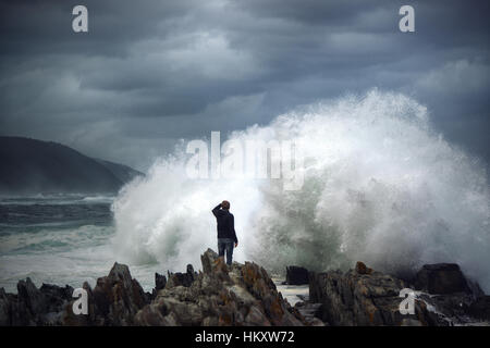 Man on rock en face de vague déferlante, surfez sur la côte rocheuse, Tsitsikamma National Park, Afrique du Sud Banque D'Images