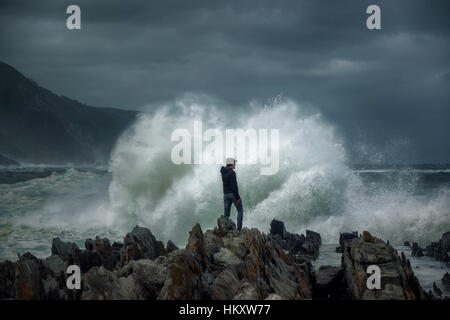 Man on rock en face de vague déferlante, surfez sur la côte rocheuse, Tsitsikamma National Park, Afrique du Sud Banque D'Images