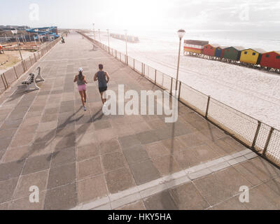 Vue arrière shot of young couple on matin tourner au promenade de la plage. Young man and woman jogging sur route le long de la plage. Banque D'Images