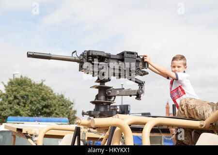 Un petit garçon posant avec un Heckler & Koch 40mm Grenade Automatique Machine Gun, au-dessus d'un désert de l'armée britannique Land Rover Banque D'Images