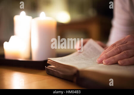 Méconnaissable woman reading Bible. Brûler des bougies à côté d'elle. Banque D'Images