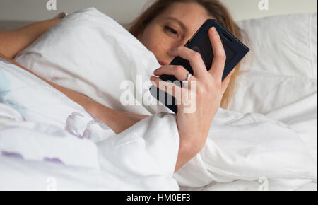 Femme au lit avec smarthphone Banque D'Images