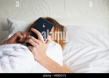 Femme au lit avec smarthphone Banque D'Images