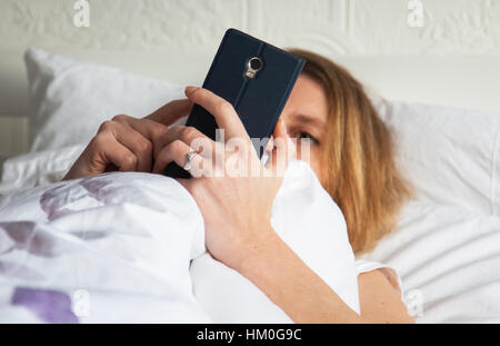 Femme au lit avec smarthphone Banque D'Images