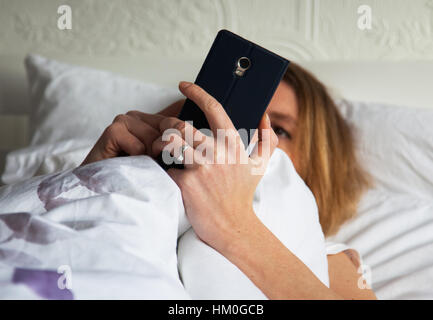 Femme au lit avec smarthphone Banque D'Images