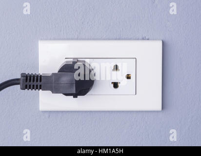 Câble noir branché dans une prise électrique blanc monté sur fond de mur gris Banque D'Images