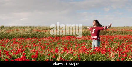 Happy Woman standing dans un champ de coquelicots rouges appréciant le paysage et de se sentir libre. Banque D'Images