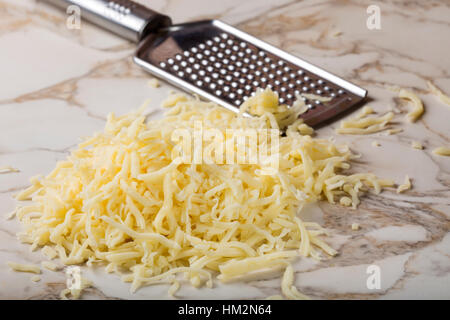 Mélanger le fromage râpé sur la table et une râpe en acier inoxydable en arrière-plan Banque D'Images