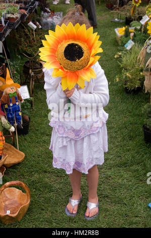 Une petite fille tenant un tournesol géant sur son visage à l'échelle nationale Garden Show, Shepton Mallet Banque D'Images