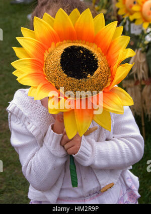 Une petite fille tenant un tournesol géant sur son visage à l'échelle nationale Garden Show, Shepton Mallet Banque D'Images