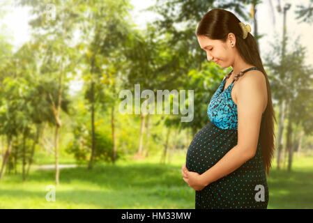 Asian pregnant woman touching her belly avec mains posant dans le parc Banque D'Images