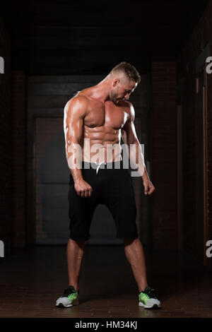 Beau jeune homme debout forte dans la salle de sport et Flexing Muscles musculaire - Fitness Model Posing Bodybuilder athlétiques exercices après Banque D'Images