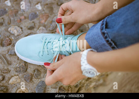 Women's Hands avec une manucure rouge lacets noués sur des chaussures d'athlétisme. Le pied se dresse sur la frontière de pierres de la mer. Marche le long de la côte en été. Sur Banque D'Images