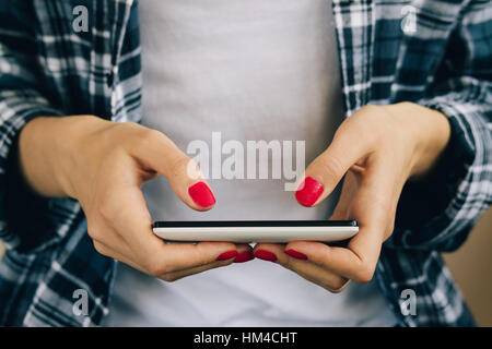 Femme en chemise à carreaux rouge et blanc manucure holding cell phone avec deux mains Banque D'Images