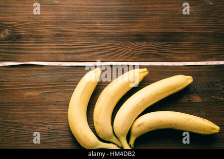 Plusieurs bananes se situent sur une table en bois à côté d'un ruban à mesurer. Vue de dessus, copy space Banque D'Images