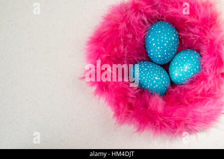 Moucheté bleu oeufs de Pâques dans un nid de fourrure rose sur fond blanc, vue du dessus Banque D'Images